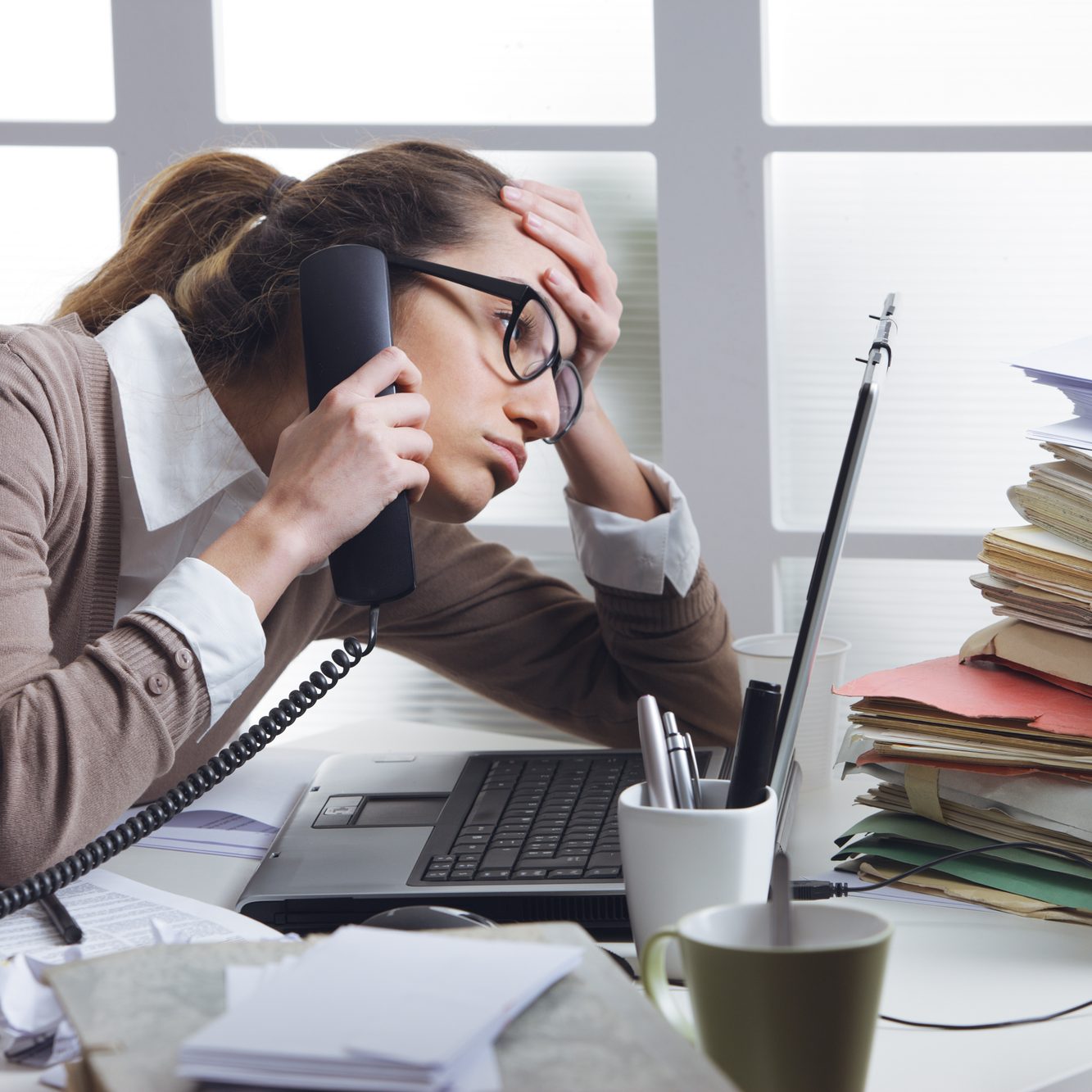 A stressed business woman looks tired  she answer telephones in her office